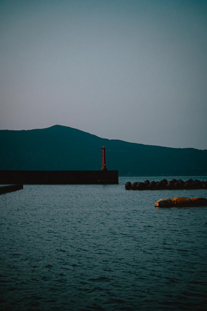 三重県答志島の港に建つ赤い灯台と防波堤、黄色いブイ