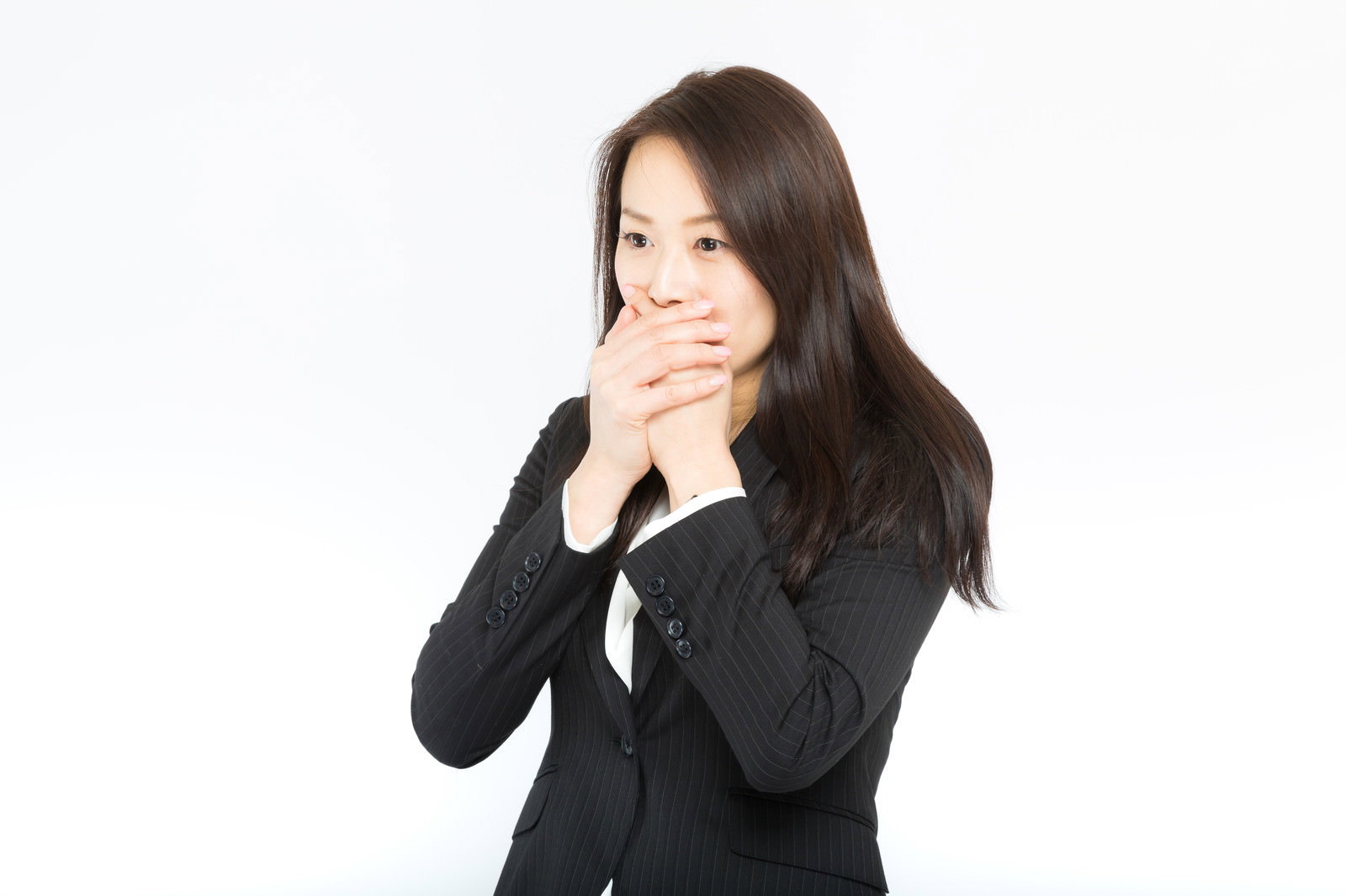 黒いスーツを着た女性が手で口を押さえて驚いている様子［モデル：土本寛子］