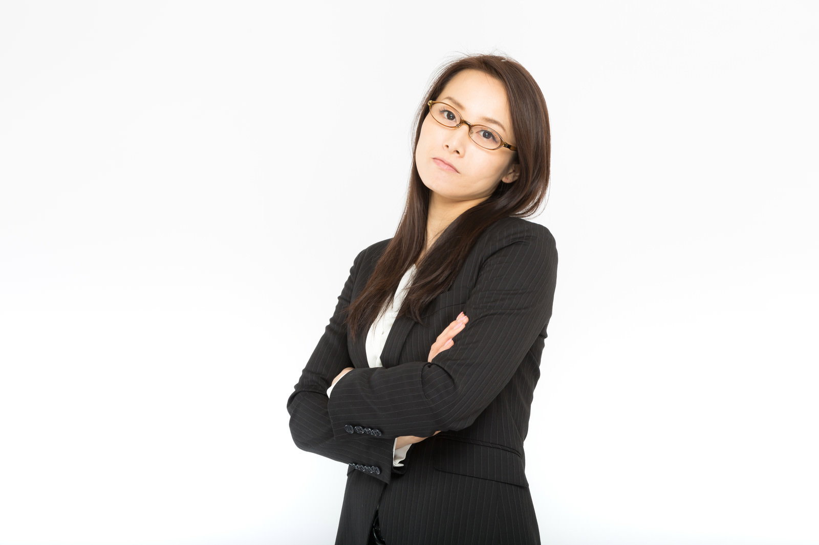 腕を組んで不満そうな表情を浮かべる黒いスーツ姿の女性社員［モデル：土本寛子］