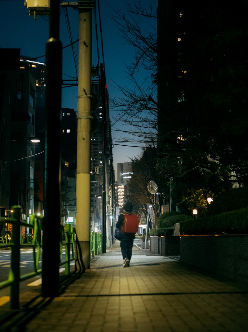 街灯に照らされた夜道を一人で歩くランドセルを背負った児童の後ろ姿