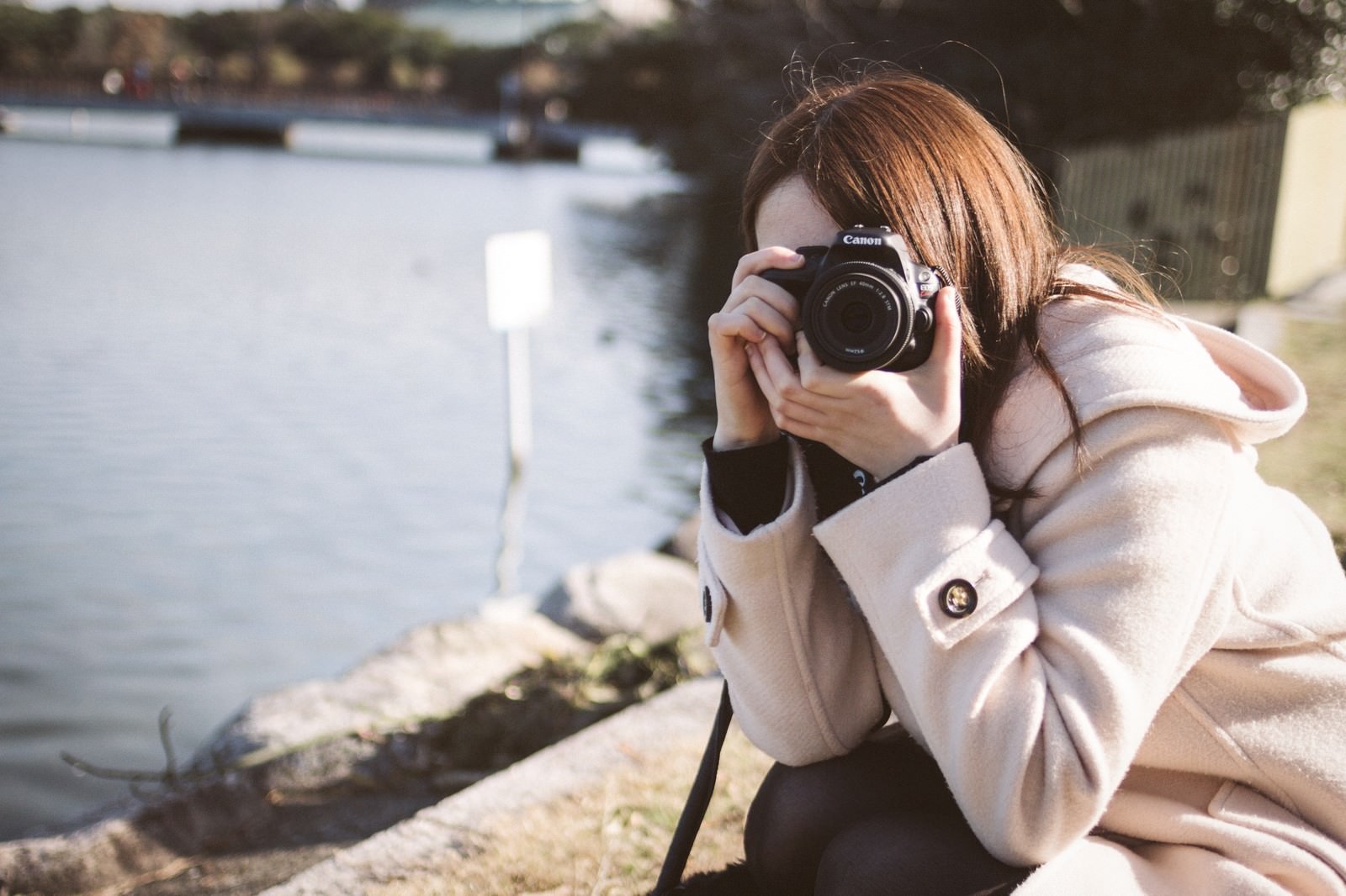 池のほとりでカメラを構えるコート姿の女性