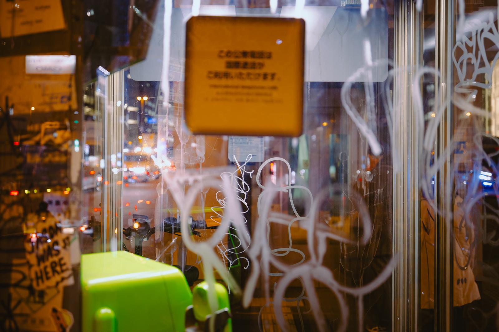 夜間の繁華街で落書きで覆われた黄色い電話ボックス