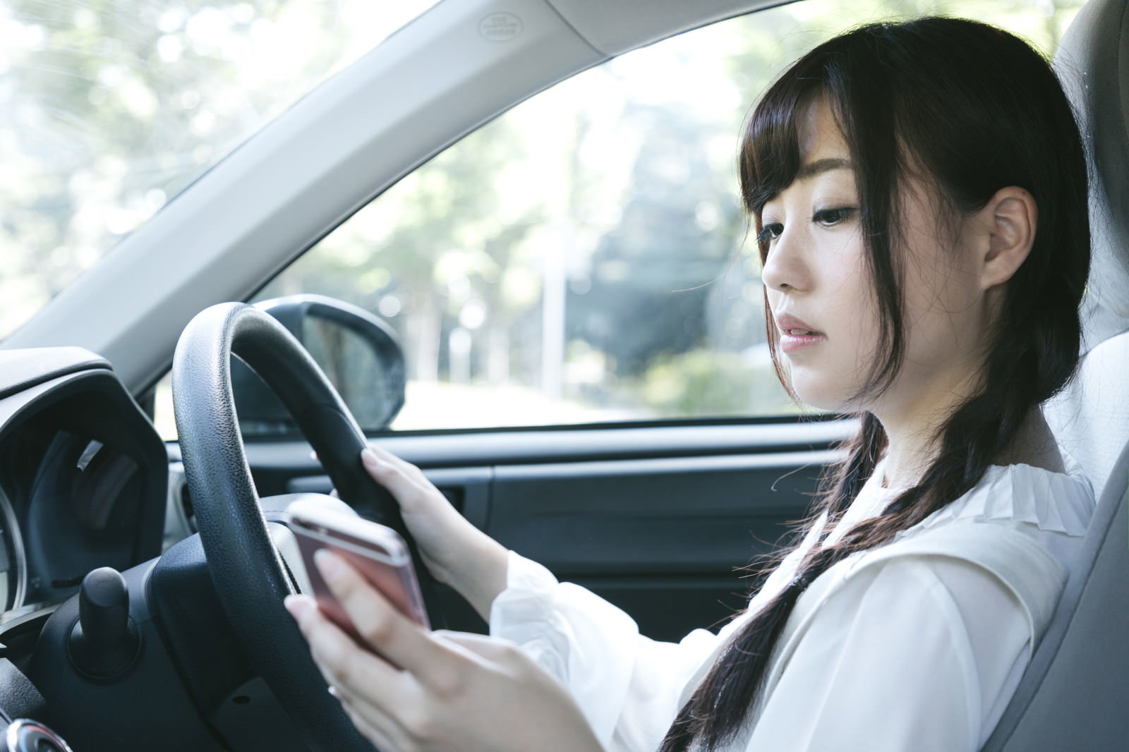 車内で運転中にスマートフォンを見ながらハンドルを握る女性［モデル：河村友歌］