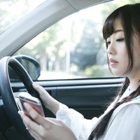 スマホを見ながら運転する女性は危険です。道路交通法違反のながらスマホの写真