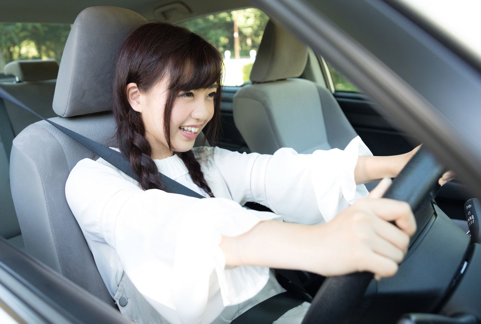 白いシャツを着た女性がハンドルを握り、車を運転している［モデル：河村友歌］