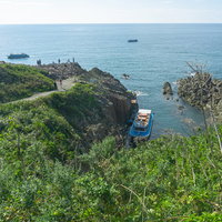 歩道から見た東尋坊観光遊覧船の乗り場に停泊中の遊覧船と沖を行く遊覧中の船の写真