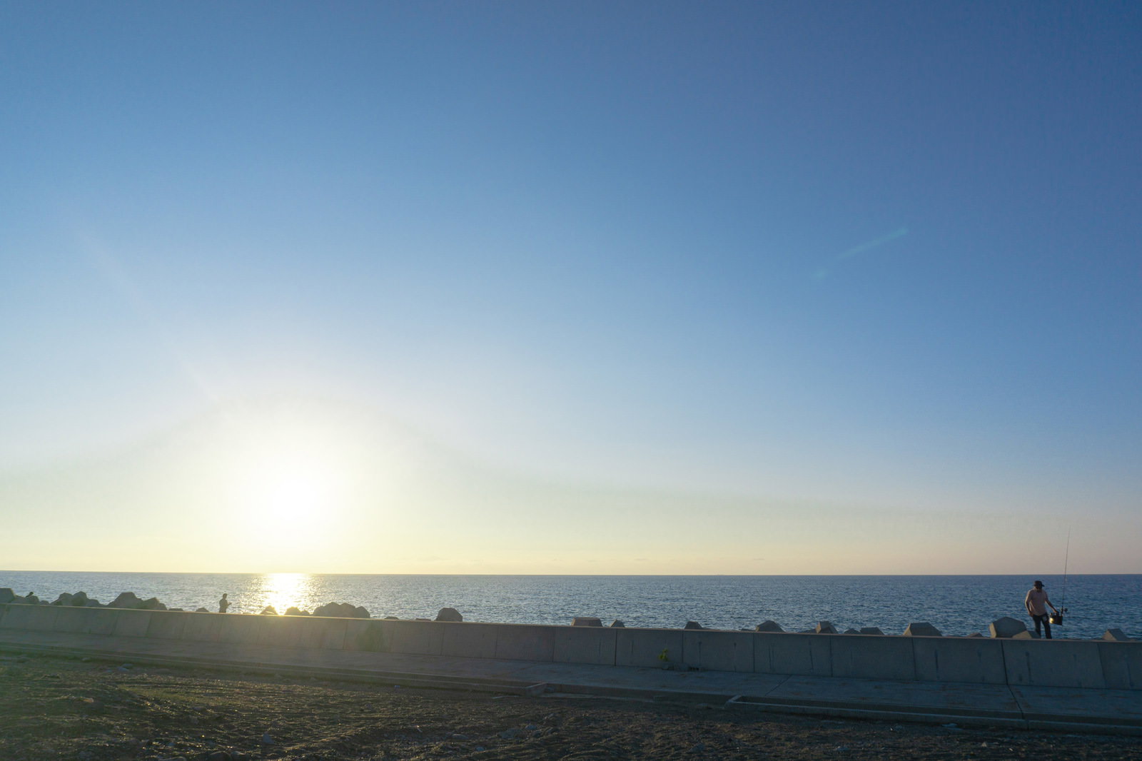 堤防のテトラポッドの上で釣りをする人と沈む太陽
