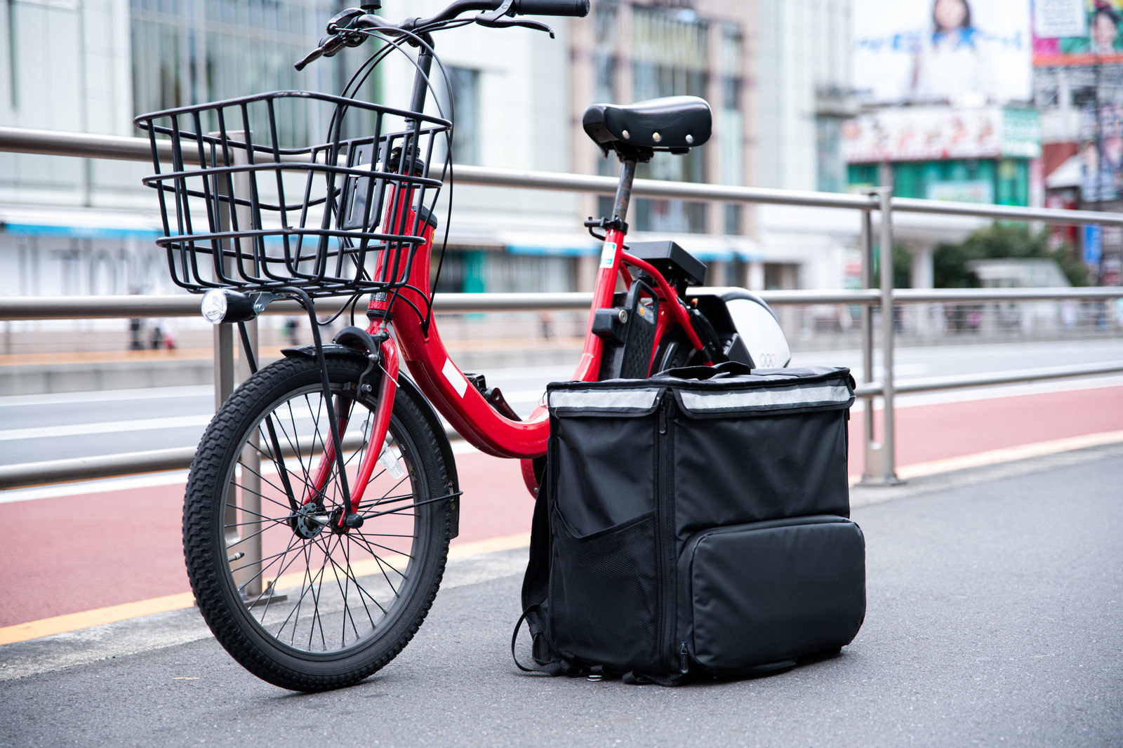 歩道に停められた赤い自転車とフードデリバリー用の黒いバッグ
