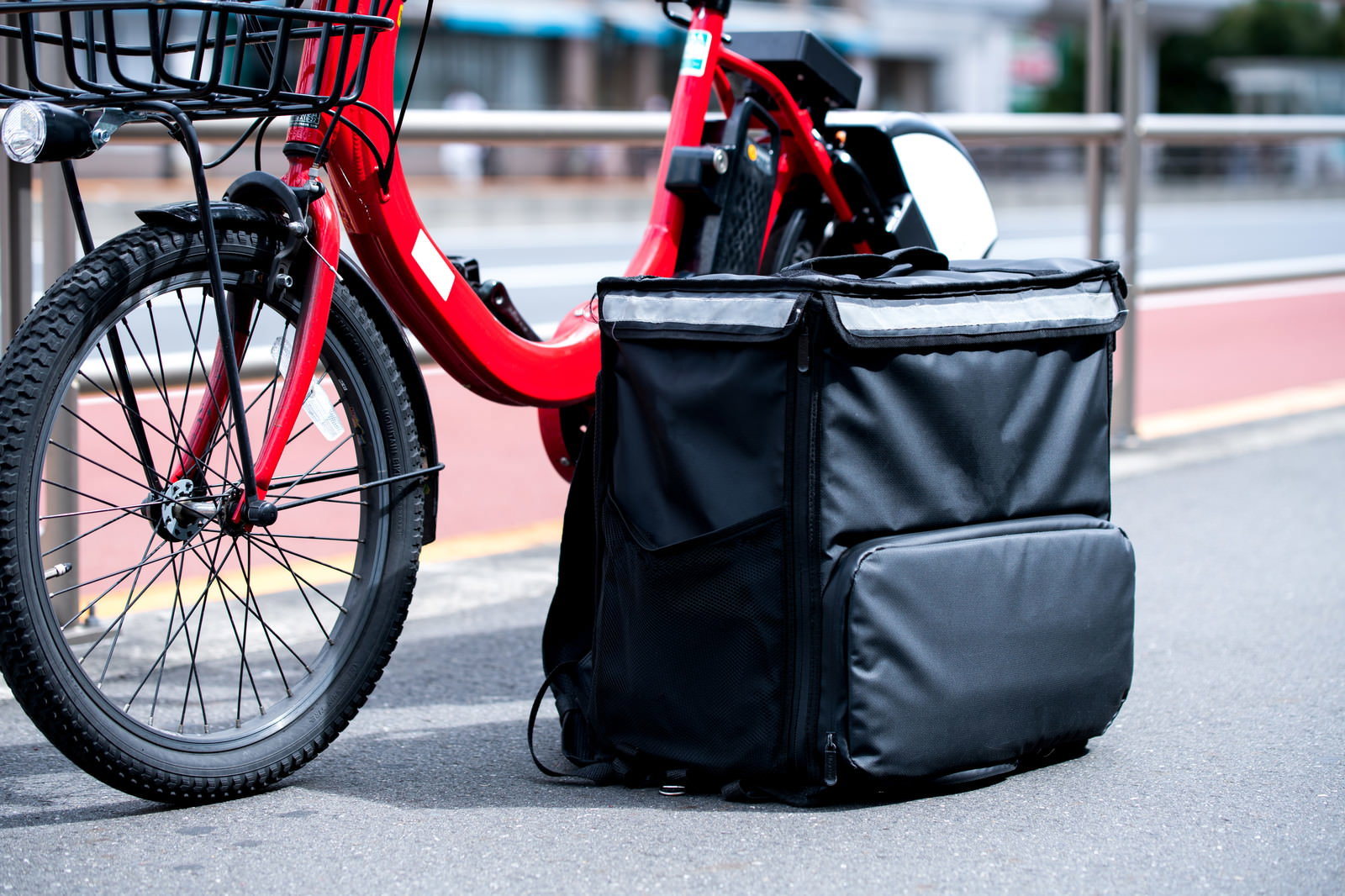 赤い自転車の前かごに設置されたフードデリバリー用の黒い保温バッグ