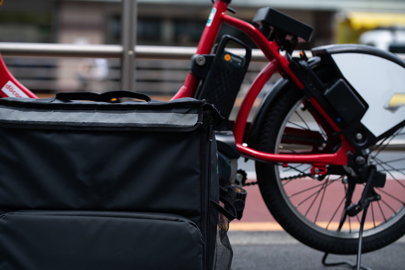 駐輪場に停められた赤い自転車の前カゴに黒いフードデリバリー用保温バッグが取り付けられている様子