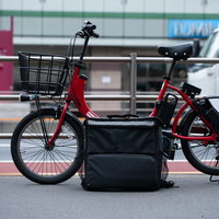 路上に停めたフードデリバリーの赤い自転車とデリバリーバッグの写真