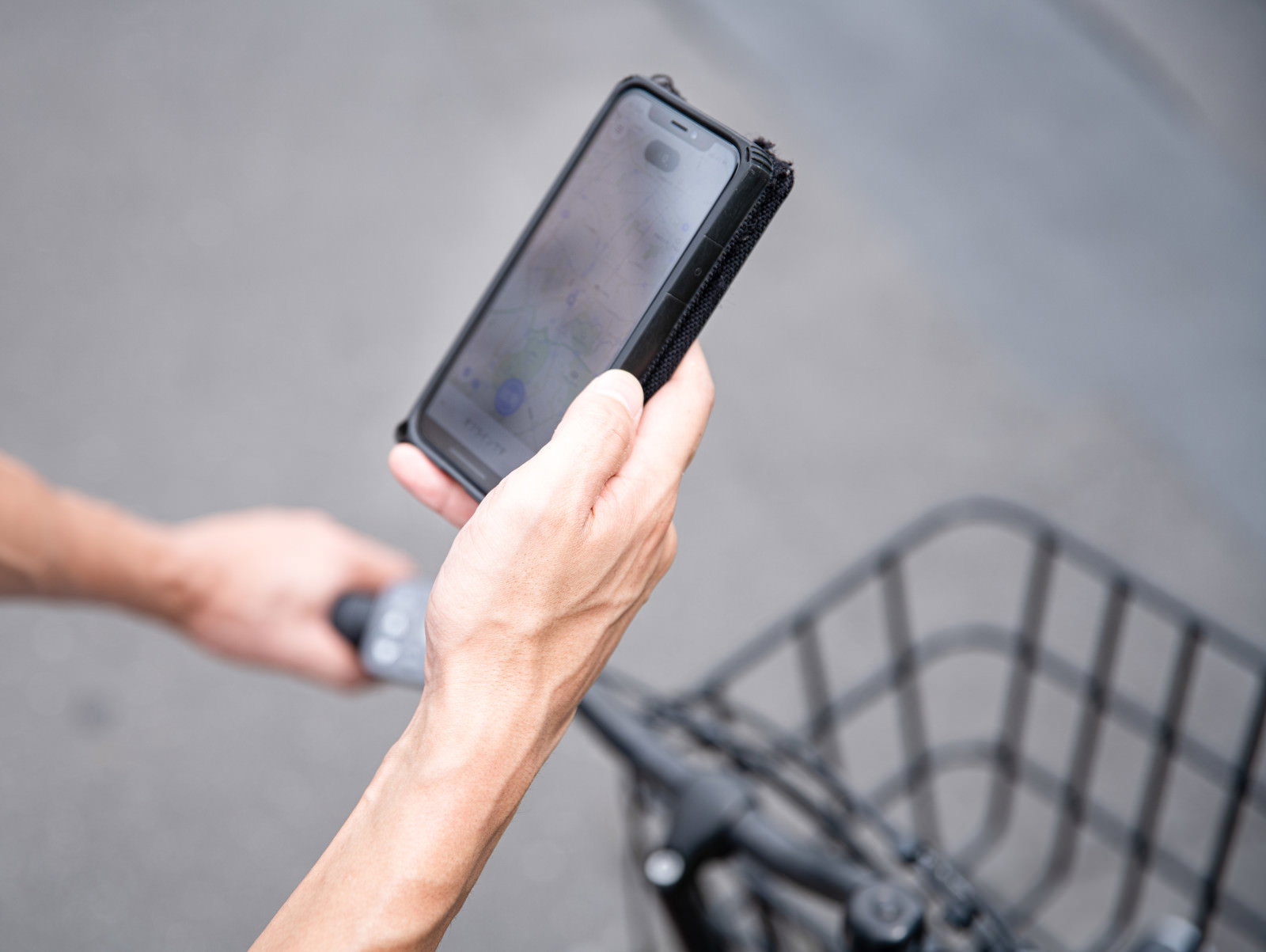 自転車のかごの横でスマートフォンの地図アプリを操作する手