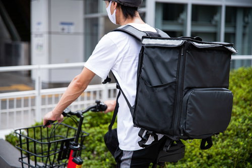 赤い自転車で配達するフードデリバリー配達員
