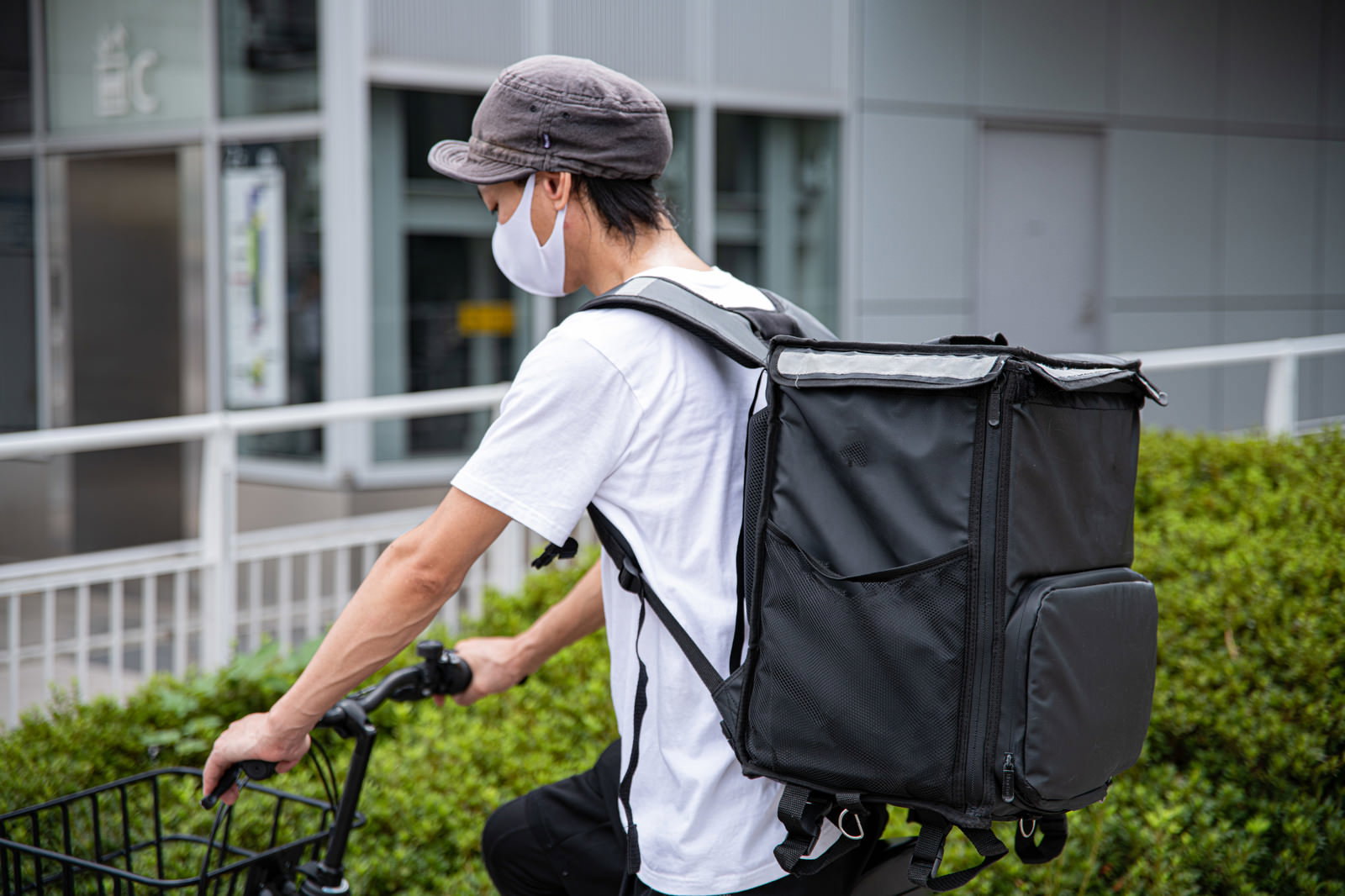 配達用バッグを背負って自転車を押す白いTシャツの男性配達員