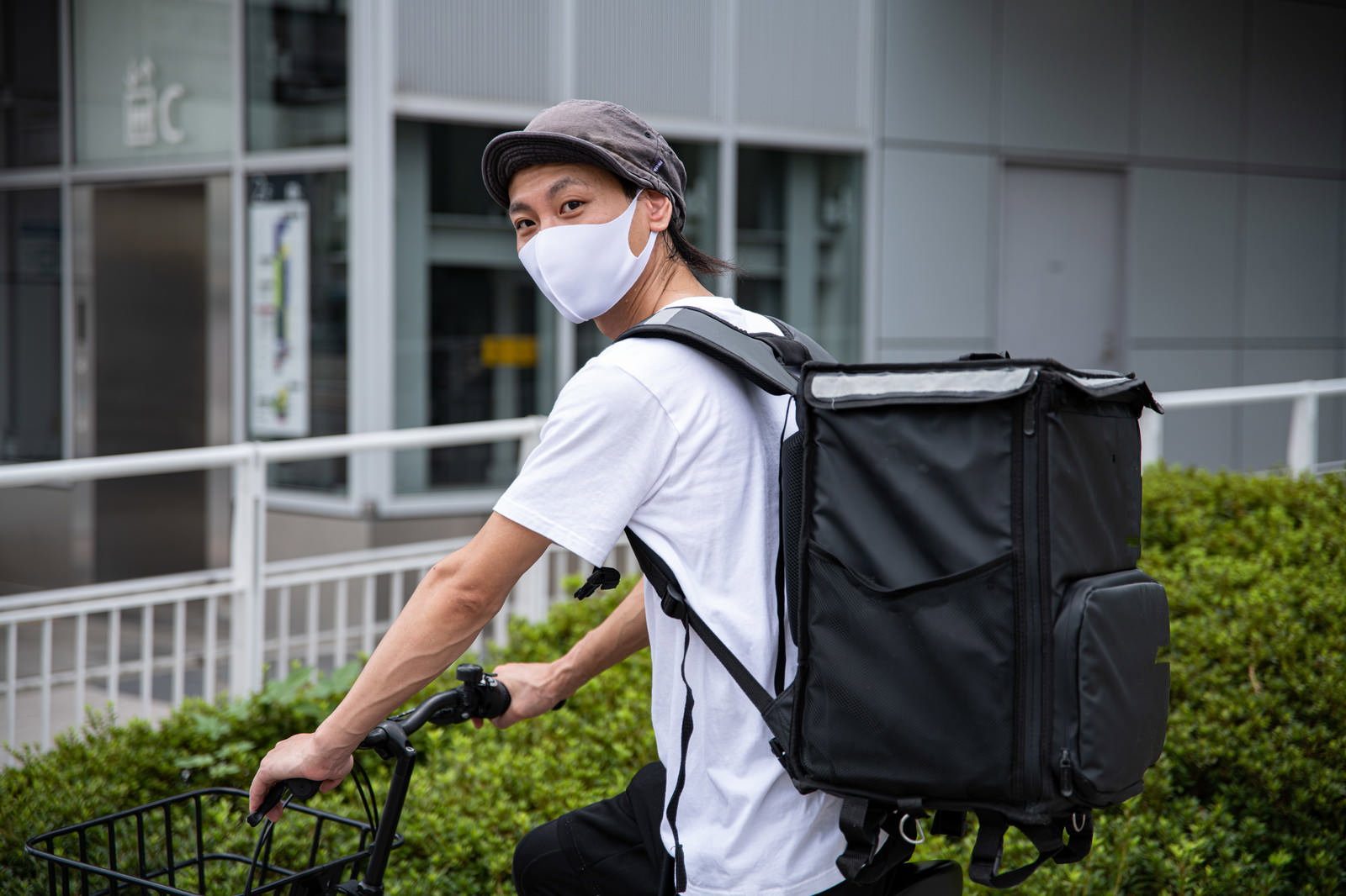 白いユニフォームを着てデリバリーバッグを背負い自転車に乗る配達員の男性