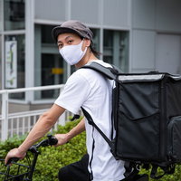 白いユニフォームを着て自転車に乗るフードデリバリー配達員の写真