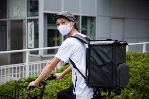 白いユニフォームを着て自転車に乗るフードデリバリー配達員