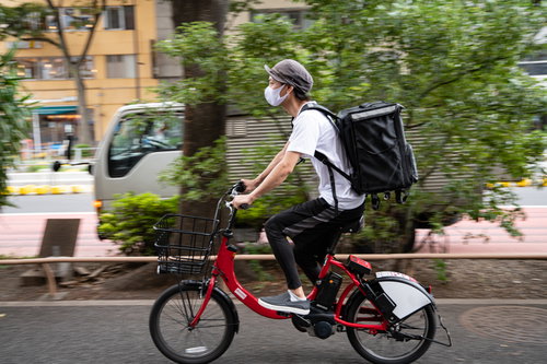 街中を走行するフードデリバリーの若い男性の写真
