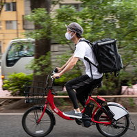 街中を走行するフードデリバリーの若い男性の写真