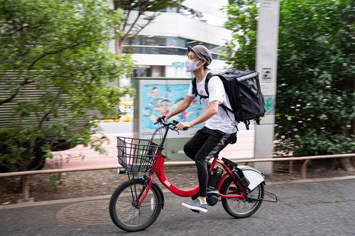 赤い自転車で配達するフードデリバリーの男性