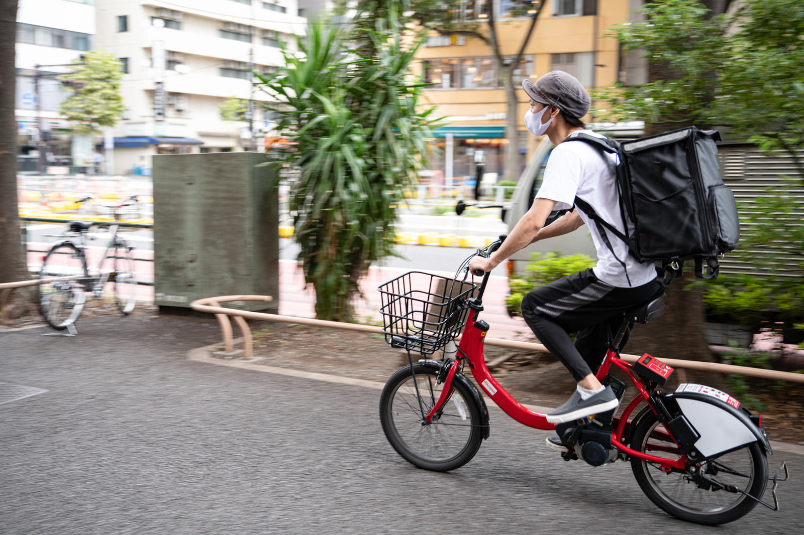 黒いリュックを背負い赤い自転車で配達業務を行う男性配達員