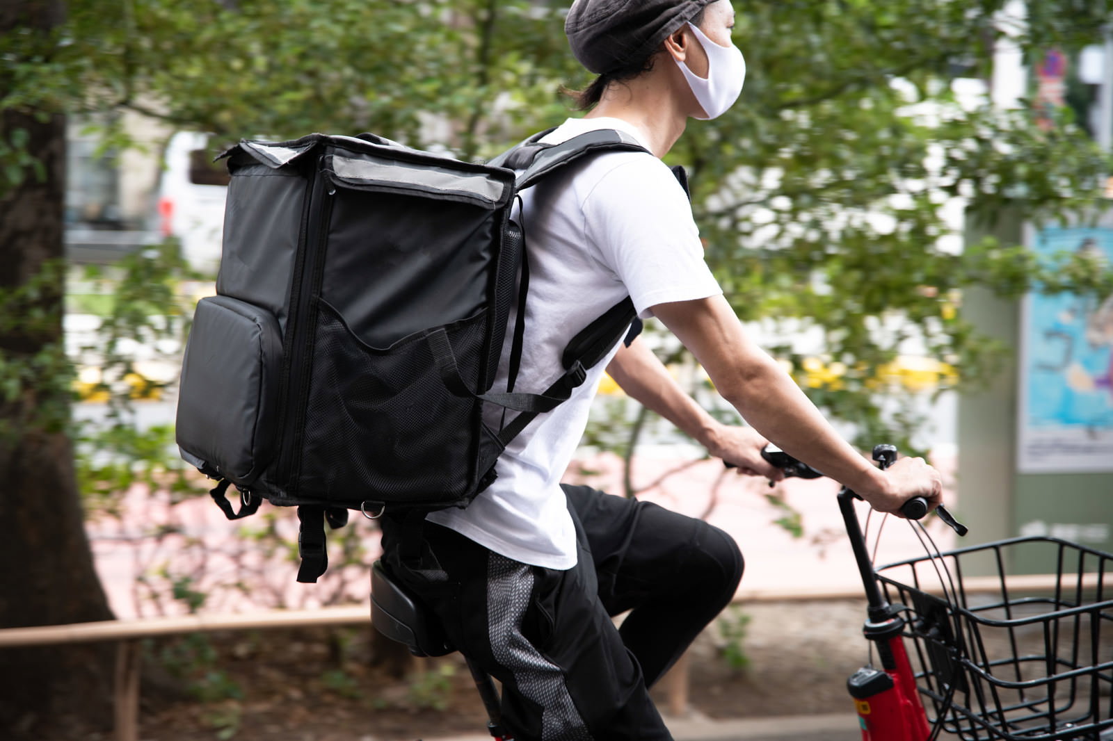 赤い自転車に乗ってフードデリバリーの配達をする男性配達員