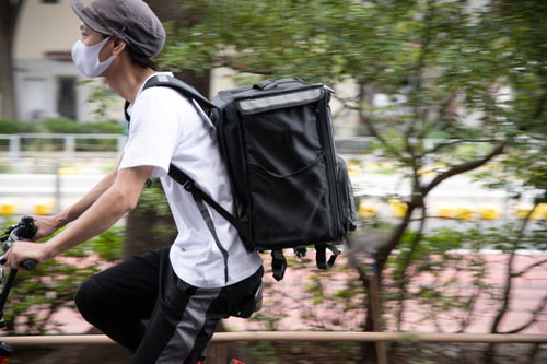 黒いリュックを背負って自転車で配達に向かう配達員