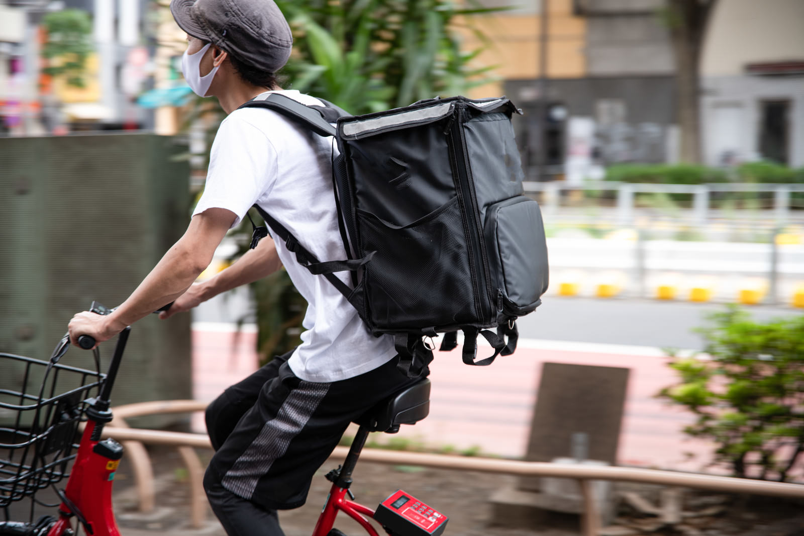 黒い配達バッグを背負い赤い自転車に乗る男性配達員