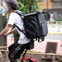 フードデリバリー特有の四角い黒いバックを背負って赤チャリに乗る配達員の写真