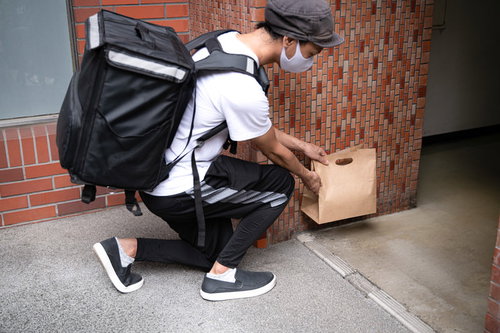 玄関先で置き配をする配達員、フードデリバリー配達業務