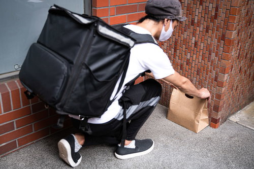玄関先に紙袋を置き配する配達パートナーの配達風景