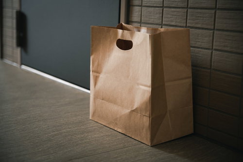 玄関前のタイル床に置き配された茶色い紙袋