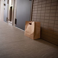 玄関前のタイル床に置かれた置き配の茶色い紙袋の写真