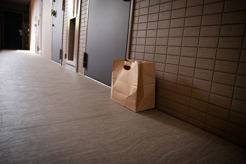 玄関前のタイル床に置かれた置き配の茶色い紙袋