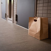 玄関前に置き配されたフードデリバリーの茶色い紙袋の写真