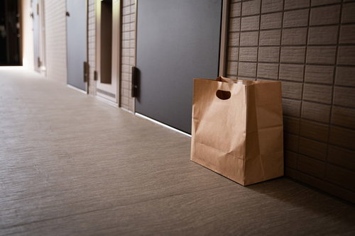 玄関前に置き配されたフードデリバリーの茶色い紙袋