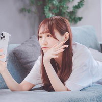 ソファーに寝転びながら白いスマートフォンで自撮りする女性の写真