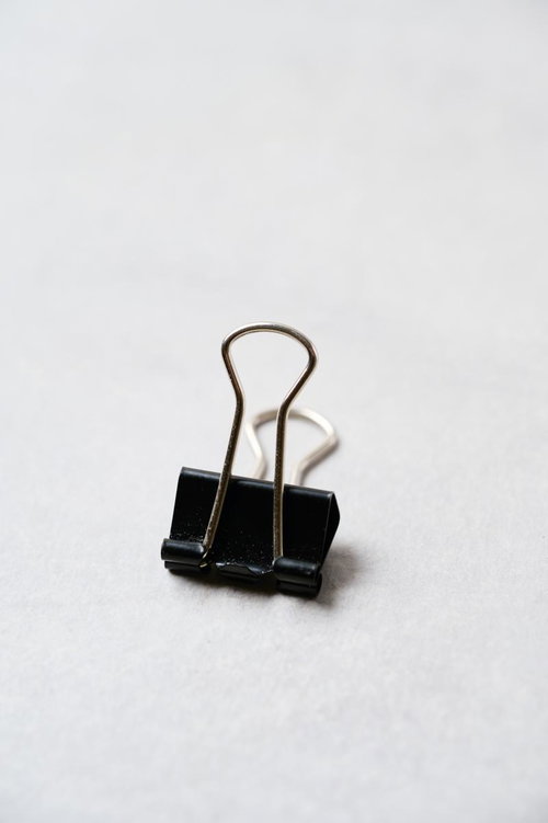 黒いバインダークリップが白い背景に置かれたシンプルなデスク用文具