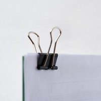 白いノートに挟んだ黒いバインダークリップの写真