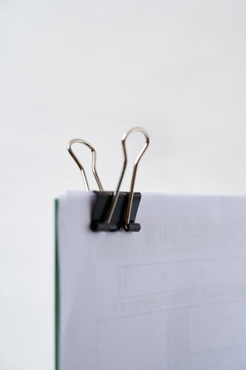 白いノートに挟んだ黒いバインダークリップ