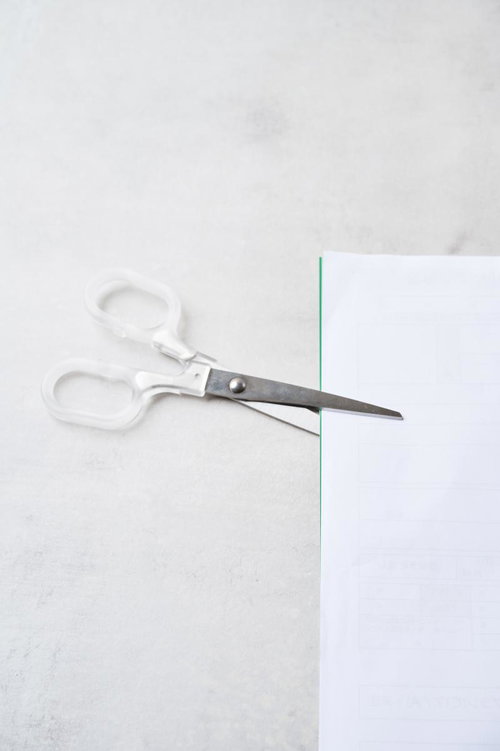 白い柄の事務用ハサミで用紙を切る作業風景