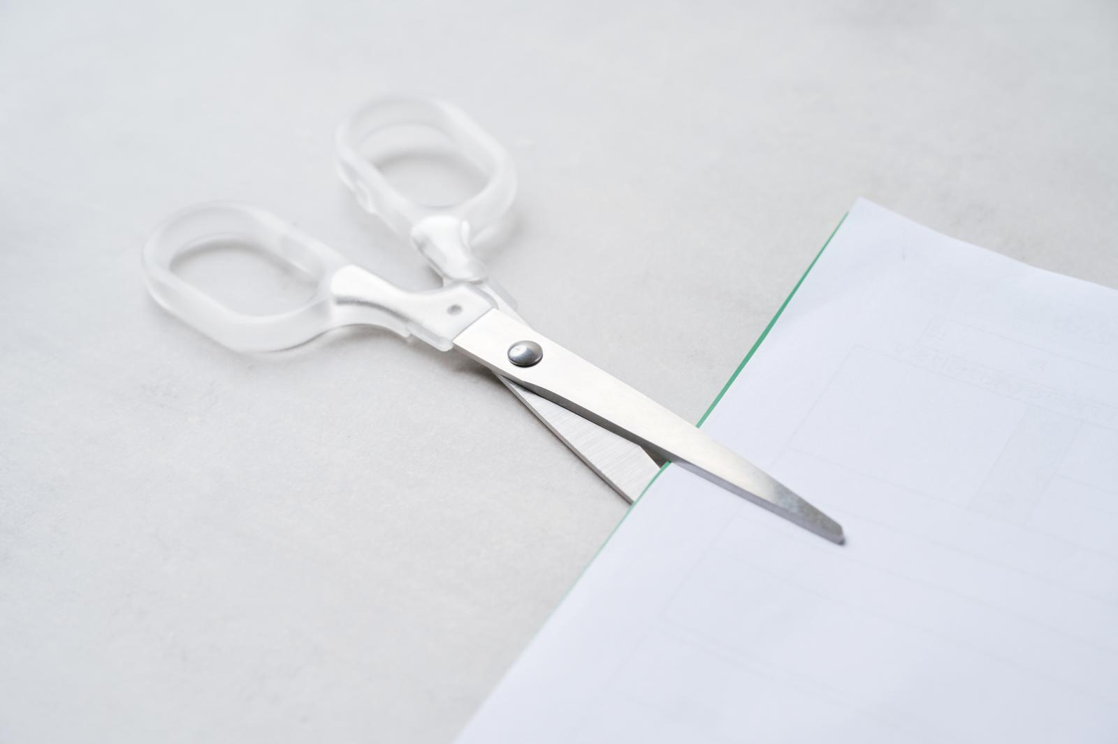 白いハサミが白い紙を切っている写真
