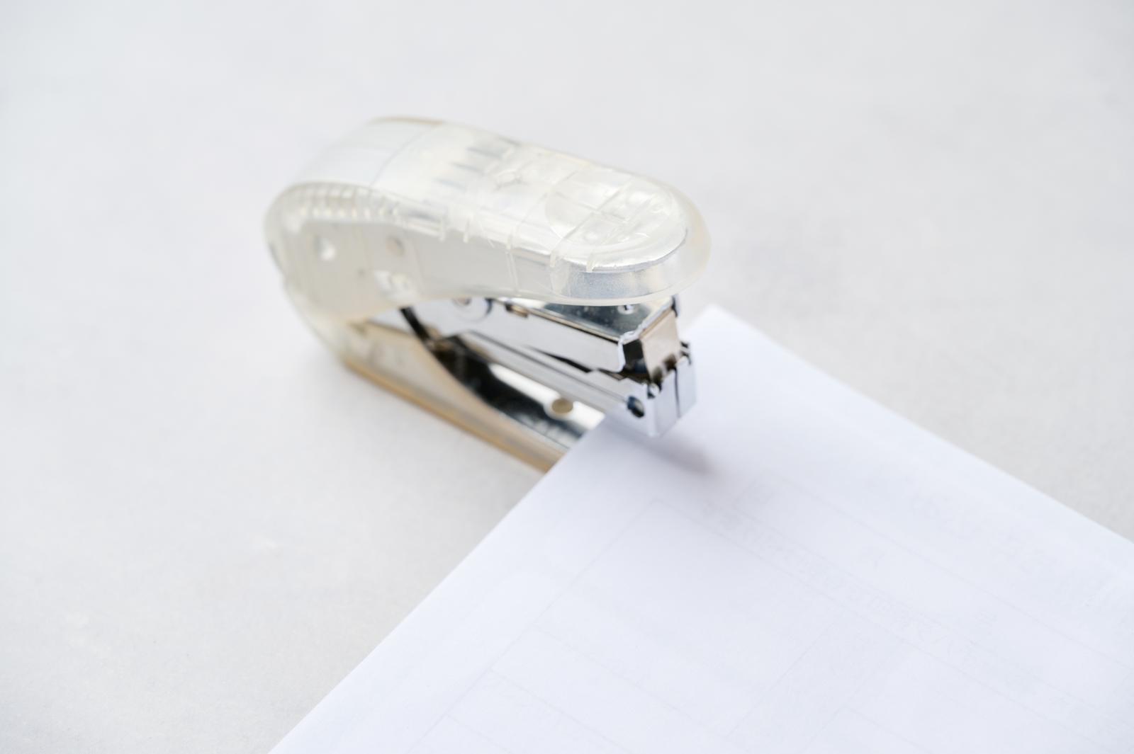 透明なボディのホッチキスで白い用紙を留めている様子