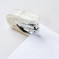 透明なボディの金属製ホッチキスで白い用紙を留めるの写真