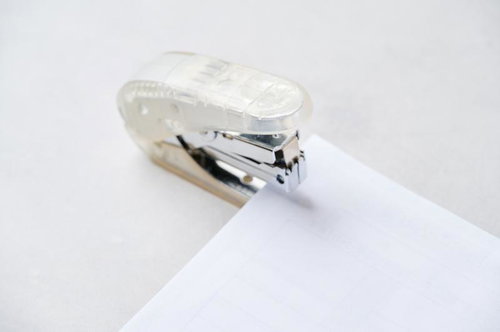 透明なボディの金属製ホッチキスで白い用紙を留める