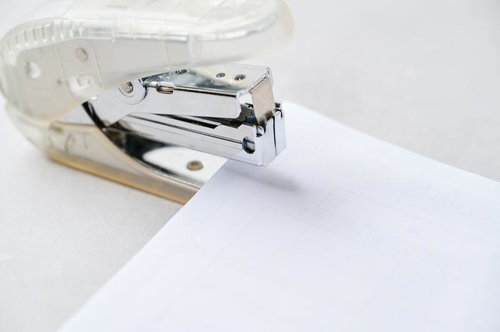 白いホッチキスで用紙の端を留める事務作業