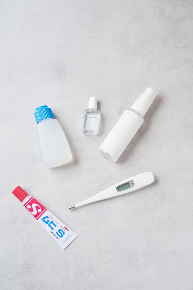 体温計、薬、スプレーボトルなど家庭の救急箱の必需品が白い背景に整列している