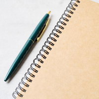 スパイラルノートと紺色のボールペンを並べたシンプルなデスクアイテムの写真