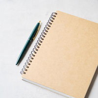 クラフト紙のスパイラルノートに添えた深緑のボールペンの写真