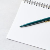 開いたスパイラルノートと緑のボールペンのセットの写真